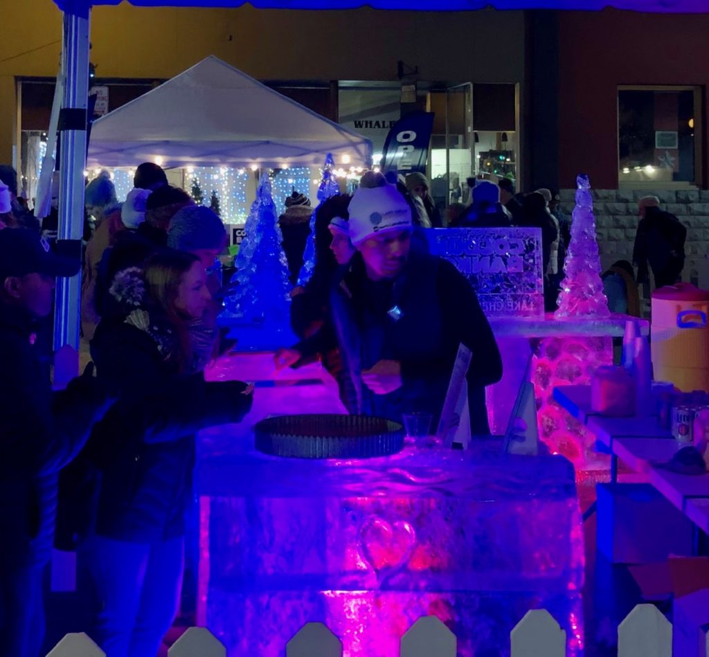 Winterfest is one of our favorite Chelan winter activities! Picture shows a man standing at a bar made of ice blocks, serving drinks to a woman.